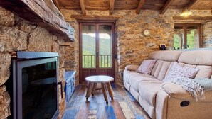 Interior rústico de una cabaña con pared de piedra, vigas de madera en el techo, un sofá, una mesita redonda y una chimenea.