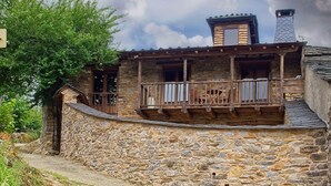Un edificio de piedra con un balcón de madera, una chimenea y una pequeña escalera que sube al nivel superior.