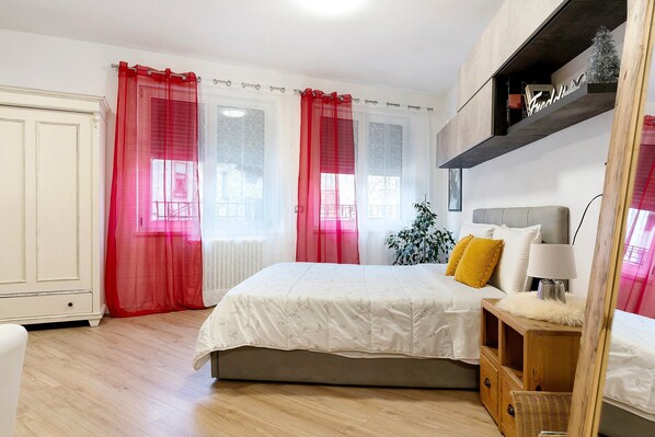 A bedroom with a bed, a nightstand, a wardrobe, and a shelf with a plant.