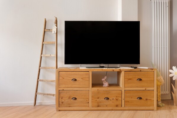 Un mueble bajo de madera para televisor con un televisor de pantalla plana, una escalera y una pequeña figurita.