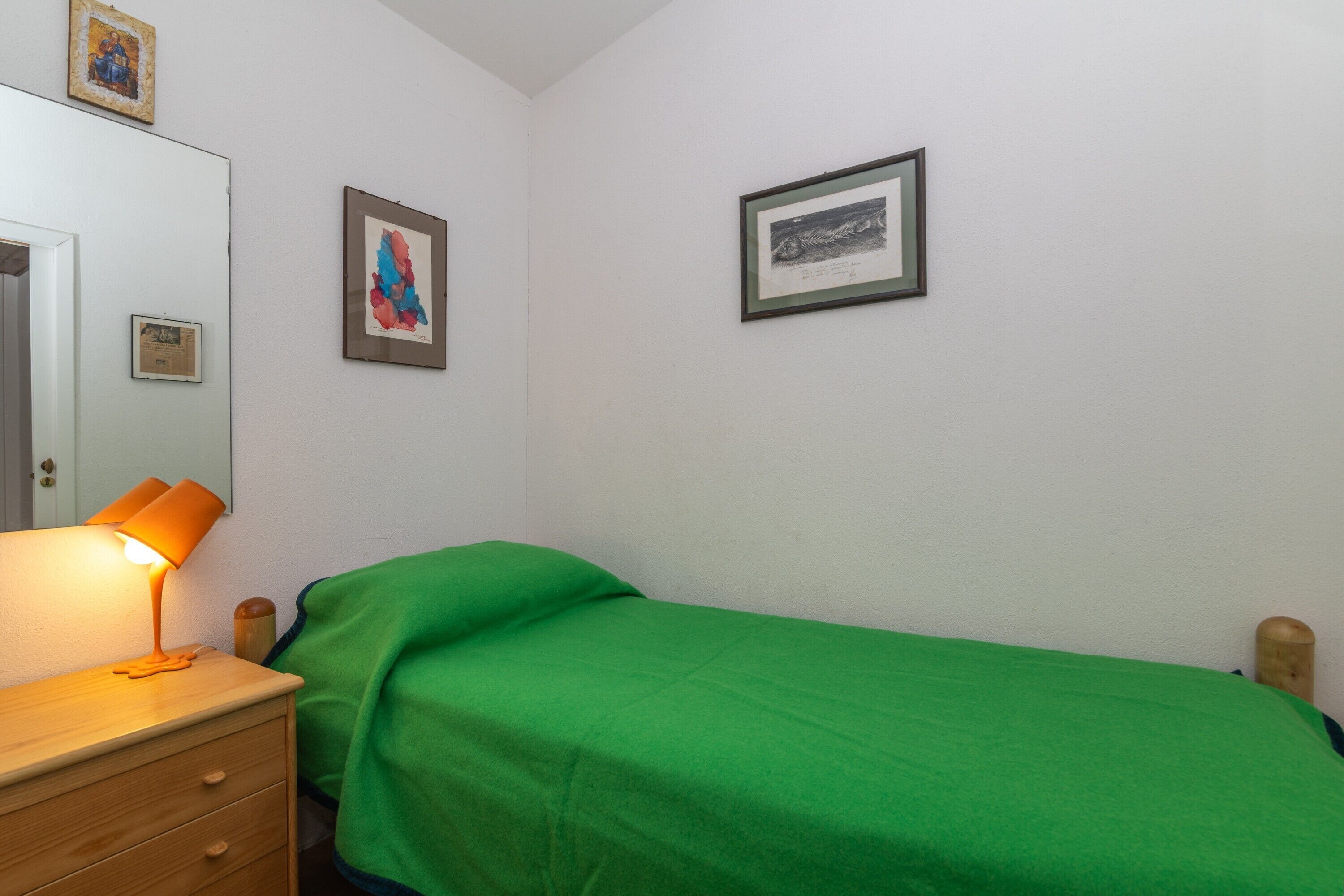 Une chambre avec un lit, une table de chevet avec une lampe et deux tableaux encadrés au mur.