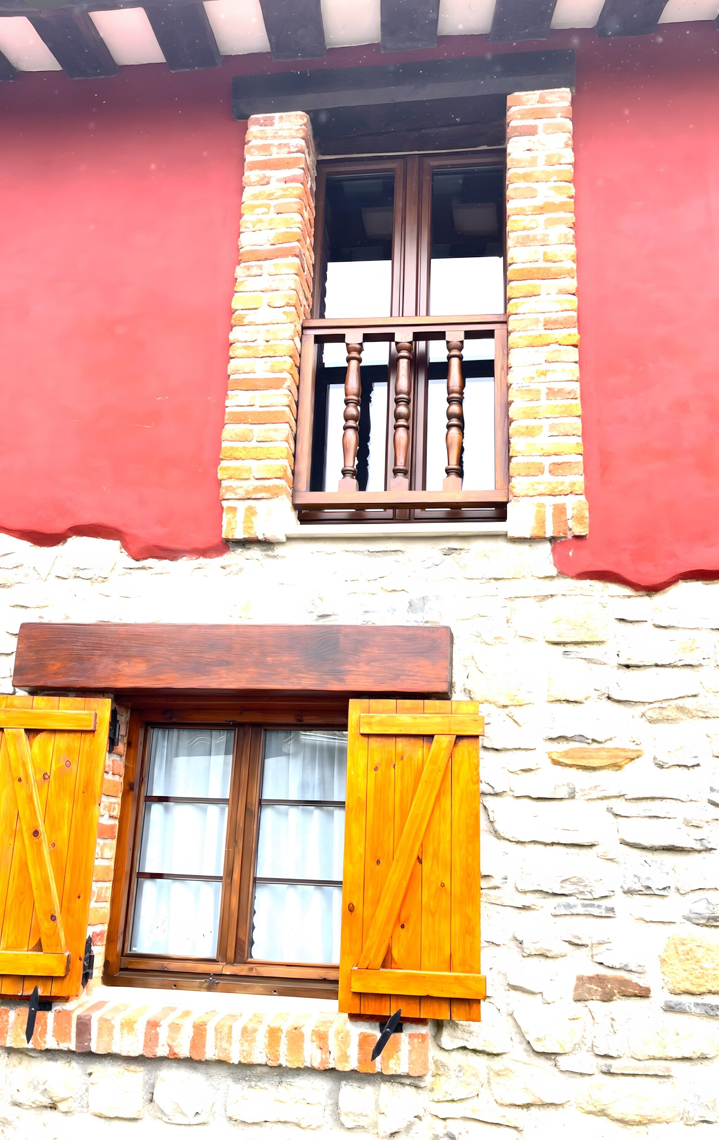 Un edificio con fachada de piedra, un balcón de madera con barandilla y una ventana con contraventanas.