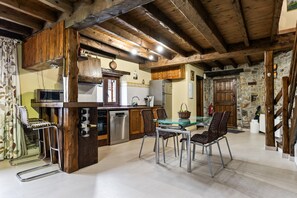 Une cuisine rustique avec des poutres en bois, un coin repas avec des chaises en osier et un mur en pierre.