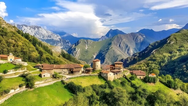 Un pueblo montañoso con edificios de piedra tradicionales, una iglesia y una vista despejada de los picos circundantes.