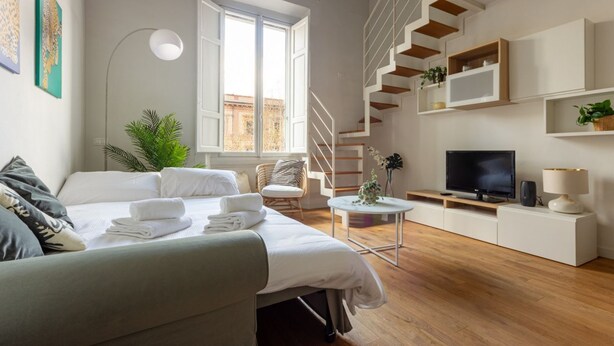 A modern hotel room with a bed, a TV, a staircase, and a window. - Libertà Bright and Stylish (Florence)