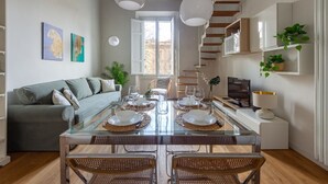 A modern living space with a dining area, sofa, TV, and staircase. - Libertà Bright and Stylish (Florence)