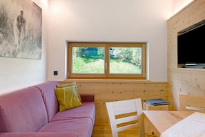 Une pièce avec un canapé rose, une table en bois, un téléviseur et une fenêtre donnant sur un paysage verdoyant.