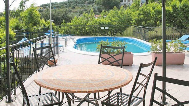 Ein überdachter Außenbereich mit Pool, Sitzgelegenheiten und Blick auf eine Hügelkulisse.