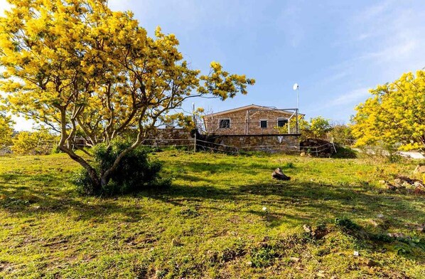 A rustic stone building with a sloped roof, surrounded by a grassy area with trees.