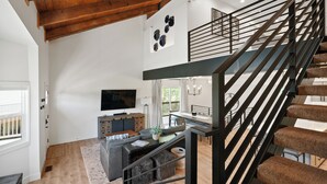 Een moderne woonkamer met een trap, houten balken, een flatscreen televisie en een eethoek.