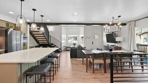 Een moderne keuken met een centraal eiland, barstoelen, hanglampen en een trap naar een hoger niveau.