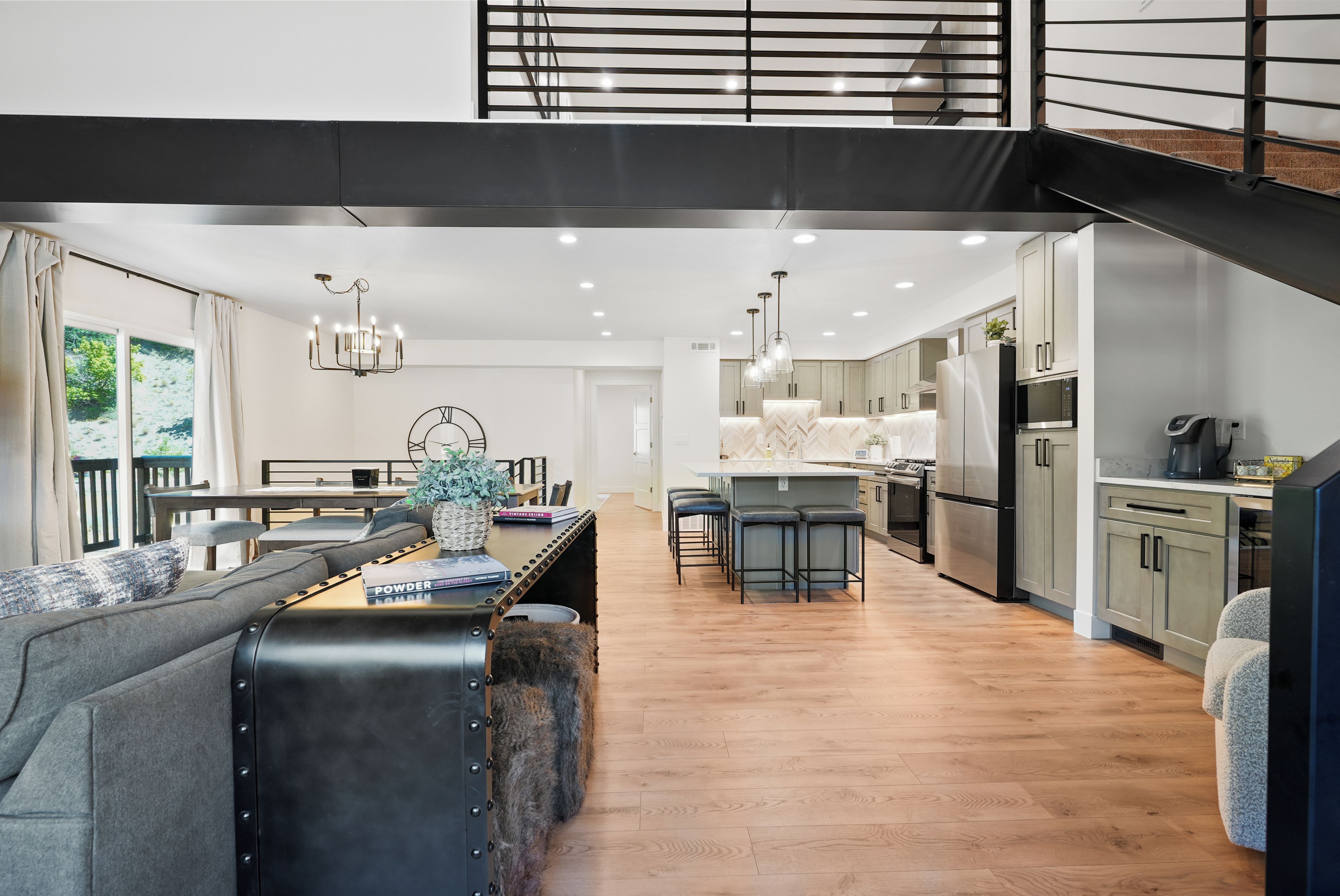 A modern kitchen with a central island, bar stools, and a dining area with a sofa and table.
