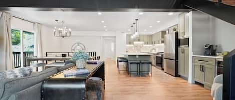 A modern kitchen with a central island, bar stools, and a dining area with a sofa and table.