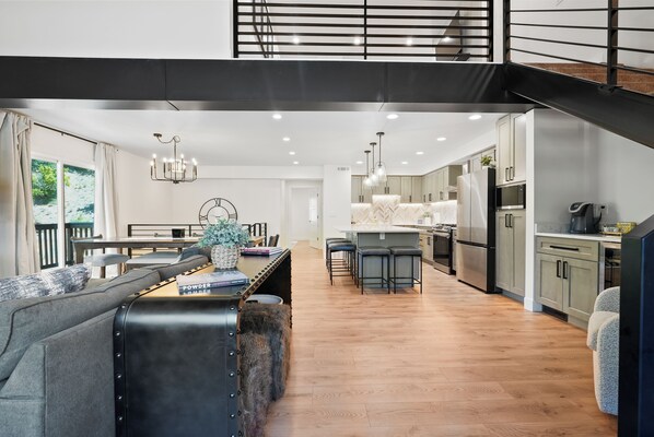 Una cocina moderna con una isla central, taburetes de bar y un comedor con sofá y mesa.