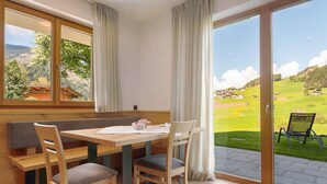 Ein Essbereich mit Holztisch und Stühlen, einer Bank und Blick auf eine grüne Landschaft durch große Fenster.