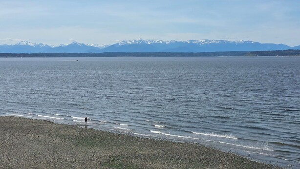 Un lac aux rives de galets, avec des montagnes enneigées qui se dressent à l'horizon.