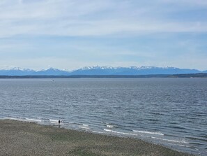 A lake with a pebbly shore and distant snow-capped mountains.