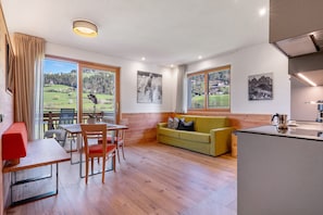 A modern room with a dining table, chairs, a sofa, and a kitchen area. - Holiday Apartment 'Baumannhof Apartment Ignis' with Mountain View, Shared Terrace and Wi-Fi (Funes)