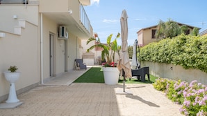 A paved courtyard with a green lawn, outdoor furniture, potted plants, and a wall with climbing plants. - Apartment 'Marzamemi 2 with Private Garden', Wi-Fi and Air Conditioning (Marzamemi)