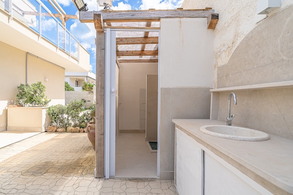 An outdoor bathroom with a shower, a sink, and a wooden pergola structure.