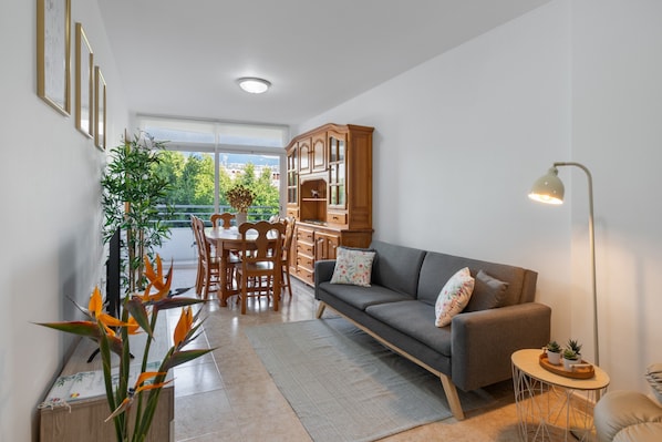 A modern living room with a sofa, a dining table, chairs, a cabinet, and a lamp.