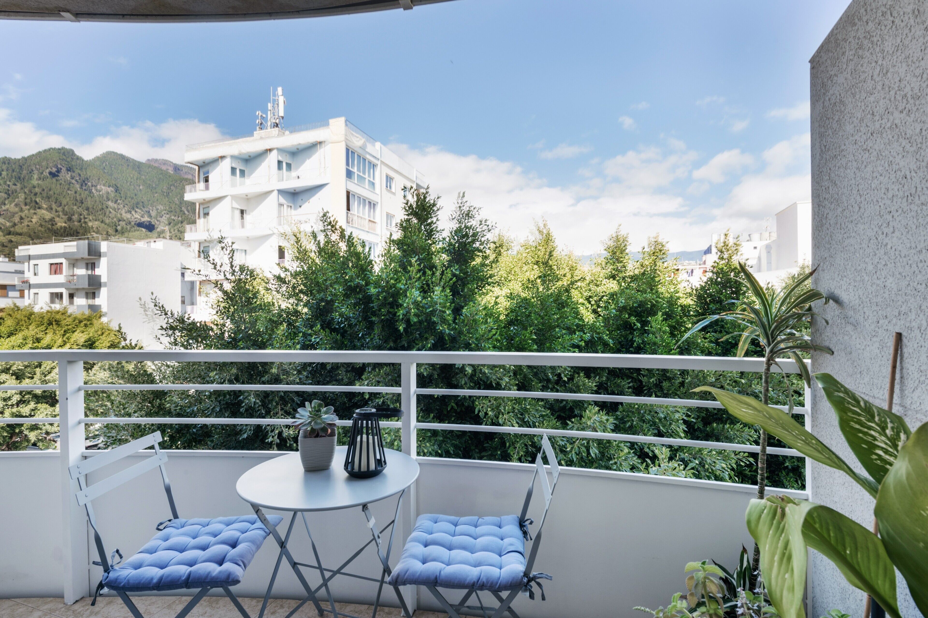 A balcony with two chairs and a table, overlooking a mountainous landscape and white buildings.