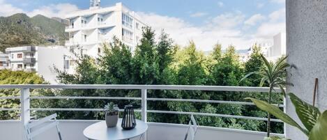 A balcony with two chairs and a table, overlooking a mountainous landscape and white buildings.
