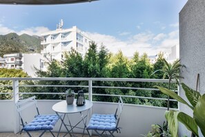A balcony with two chairs and a table, overlooking a mountainous landscape and white buildings.