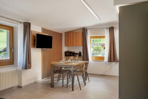 A modern dining area with a table set for four, a flat-screen TV mounted on the wall, and a view of the outdoors. - Apartment 'Rosa Blu' with Balcony and Wi-Fi (Piano)