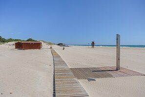 Uma praia arenosa com calçadão de madeira, cabanas e torres salva-vidas.