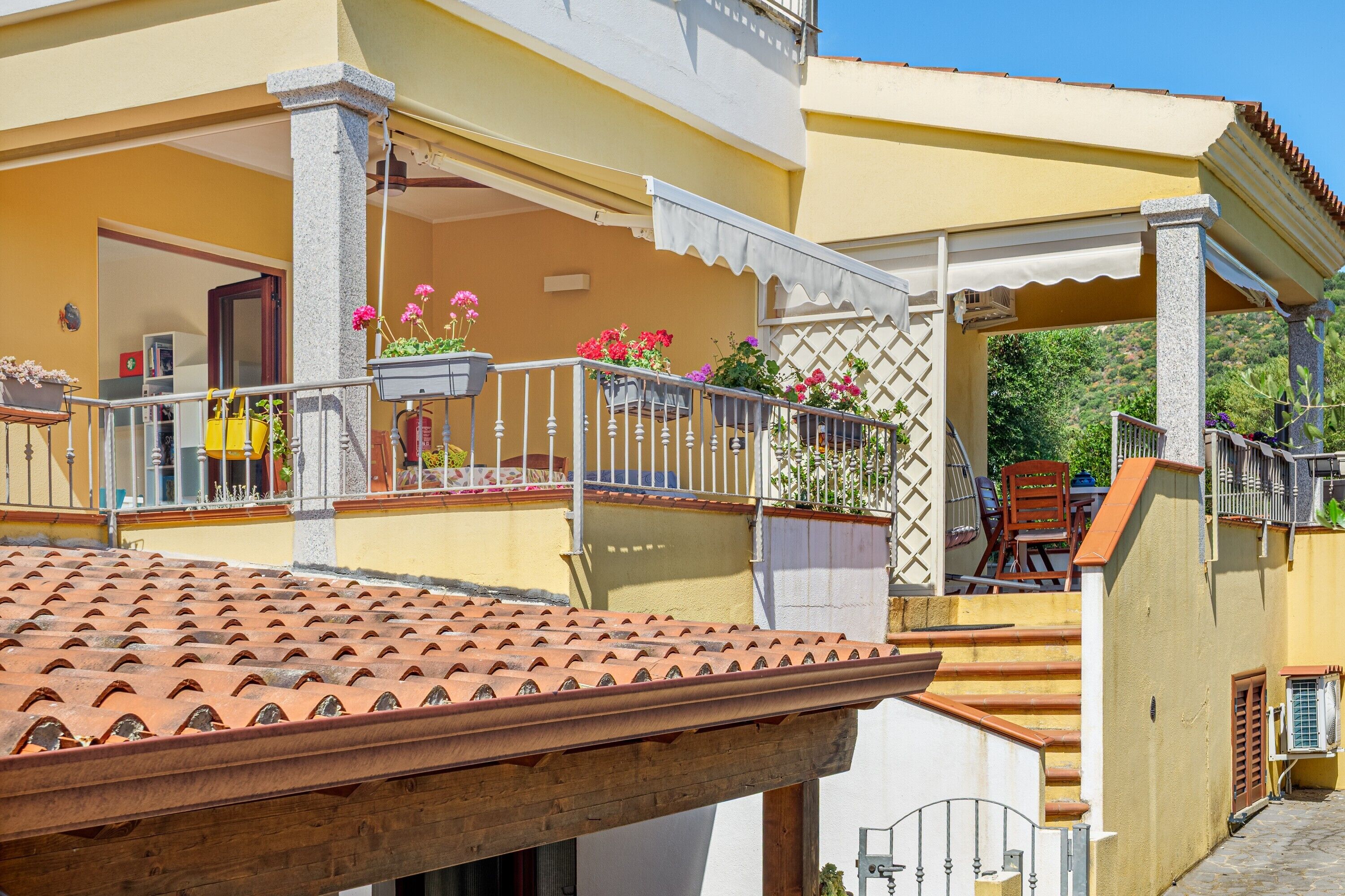 Un bâtiment jaune avec un toit recouvert de tuiles, un balcon doté de balustrades et des plantes en pot.