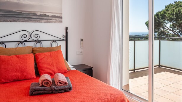 A bedroom with a bed, pillows, and towels, a nightstand, a wall-mounted power outlet, and a balcony with a view. - Holiday Home 'Azzure' with Sea View, Wi-Fi and Air Conditioning (Lloret de Mar)