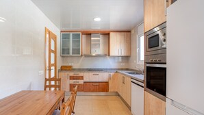 A kitchen with wooden cabinets, a stainless steel oven, and a wooden dining table. - Holiday Home 'Azzure' with Sea View, Wi-Fi and Air Conditioning (Lloret de Mar)