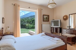 Une chambre à coucher comprenant un lit, un téléviseur, une commode et offrant une vue sur une montagne et la verdure.