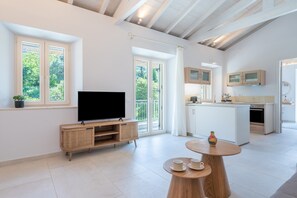Uma sala moderna com uma televisão de tela plana, um rack de madeira, uma mesa de jantar com xícaras e uma cozinha com armários brancos e forno embutido.