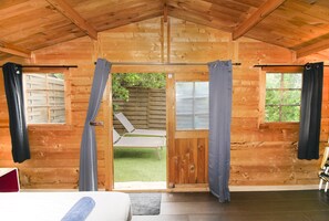 Une cabane en bois avec un lit, une porte donnant sur un balcon et une vue sur un jardin.