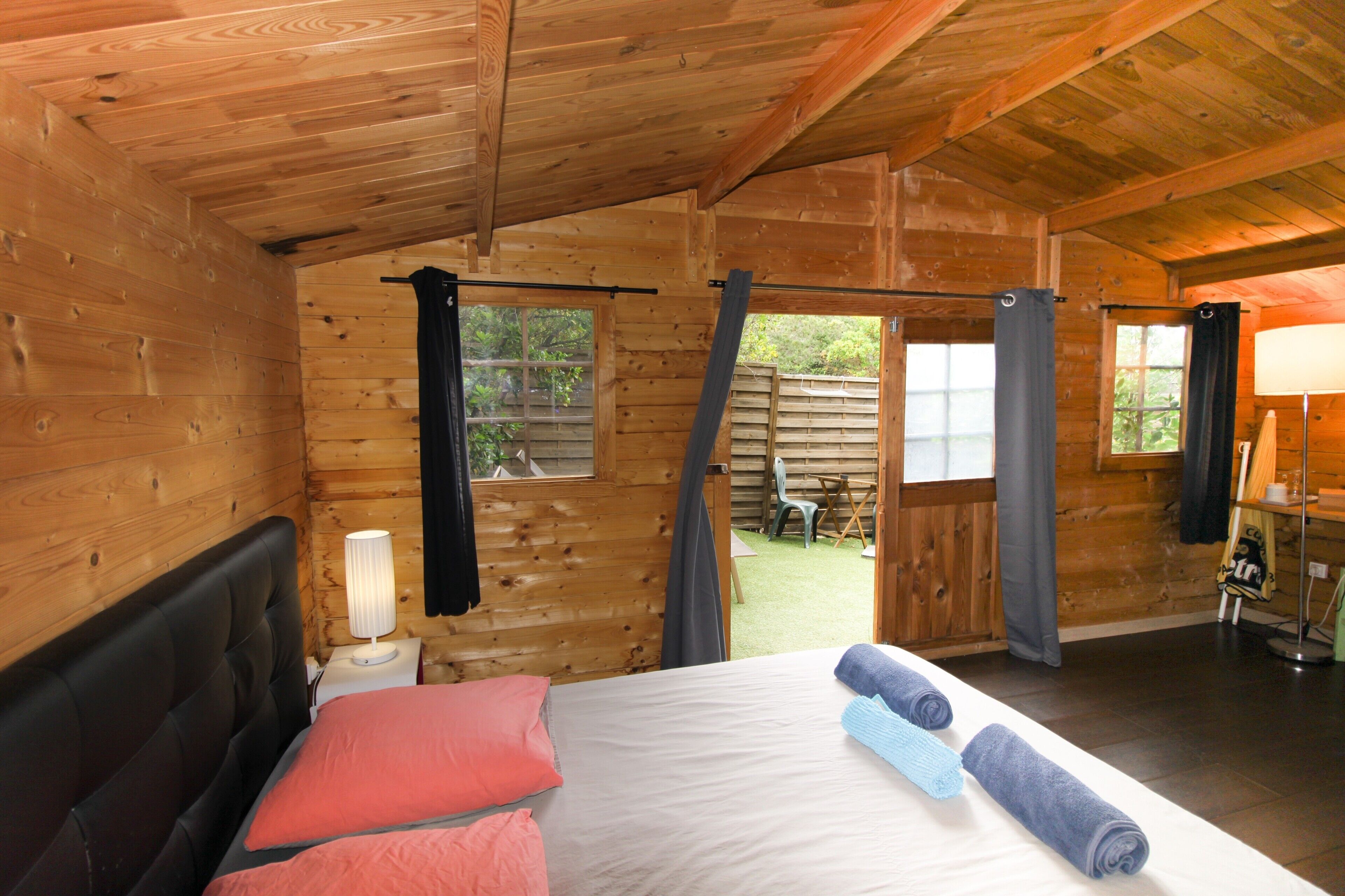 Una habitación de cabaña de madera con una cama, una mesita de noche, una ventana y vistas al exterior.