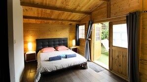 A wooden-paneled bedroom with a bed, nightstands, and a view through a sliding door. - Chalet 'De La Plage U Tempu' with Sea View, Wi-Fi and Air Conditioning (Coti-Chiavari)