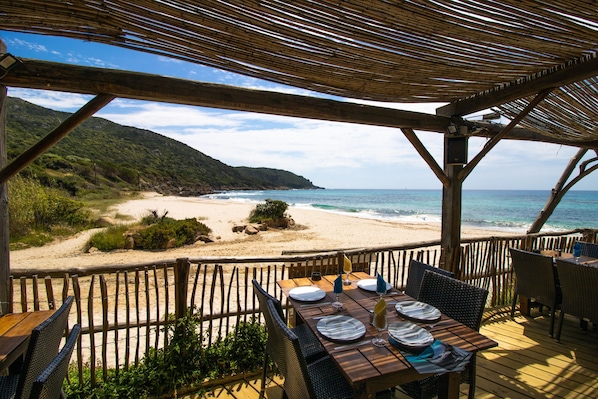A wooden deck with a table set for dining, overlooking a beach and ocean.