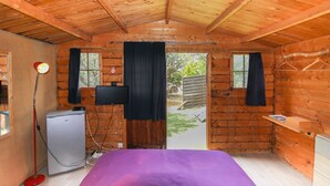 A wooden cabin room with a bed, a small refrigerator, a television, and a window with curtains. - Chalet 'De La Plage Serena' with Sea View, Wi-Fi and Air Conditioning (Coti-Chiavari)
