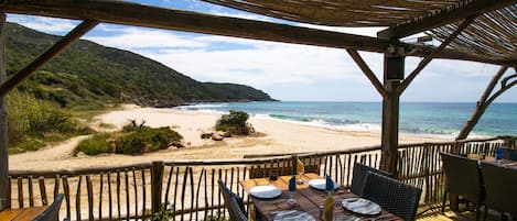 A wooden deck with a table set for dining, overlooking a beach and ocean.