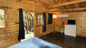 Una habitación de cabaña de madera con una cama, un escritorio, un televisor y una ventana.
