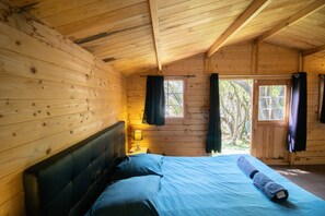 A wooden cabin bedroom with a bed, a nightstand, a window, and a door.