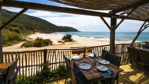 Une terrasse en bois avec une table dressée pour le dîner, offrant une vue sur la plage et l’océan.