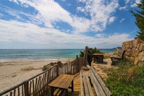 A wooden deck leading to a beach with a rocky outcrop and a bench.