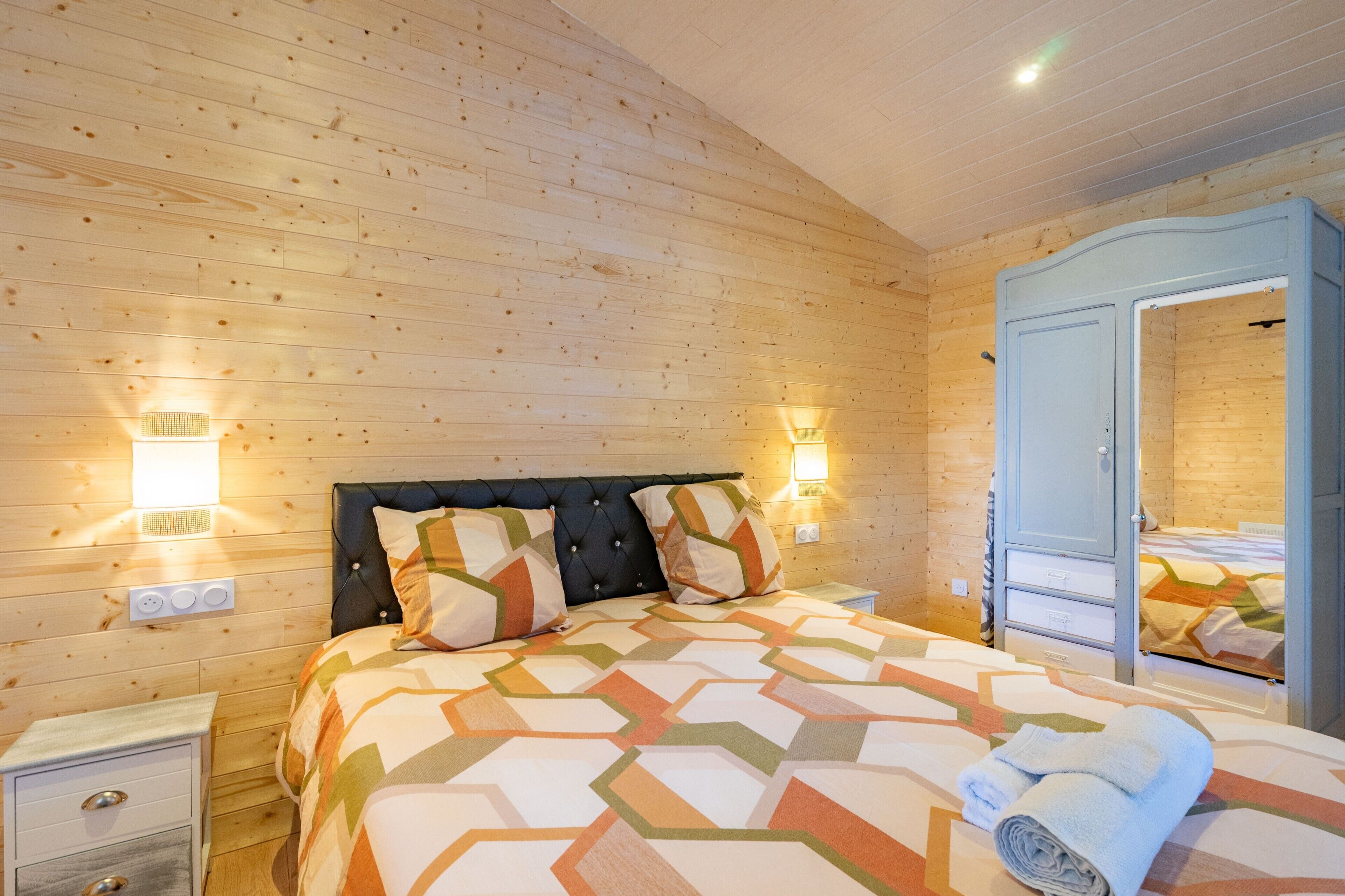 Een kamer met houten lambrisering, een bed, bedlampen, een kast en een spiegel.