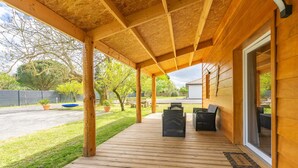 Eine Holzterrasse mit Gartenmöbeln, ein überdachter Bereich und Blick auf eine Straße und Grünflächen.