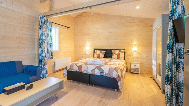 Ein Zimmer in einer Holzhütte mit einem Bett, einer Couch, einem Fernseher und einem kleinen Nachttisch.