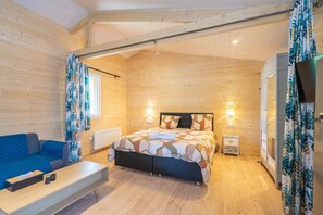 A wooden cabin room with a bed, a sofa, a TV, and a small bedside table.
