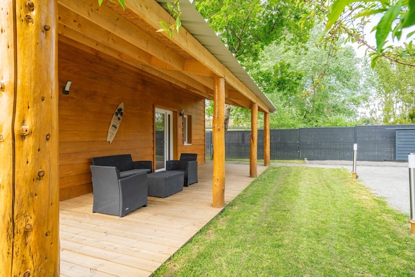 A covered outdoor area with wooden beams, a grassy lawn, and a patio with seating.
